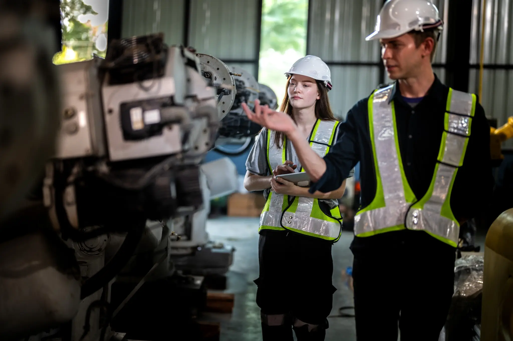 Dos técnicos con cascos y chalecos de seguridad inspeccionando maquinaria industrial dentro de una fábrica, representando un entorno técnico relacionado con cursos de AutoCAD.